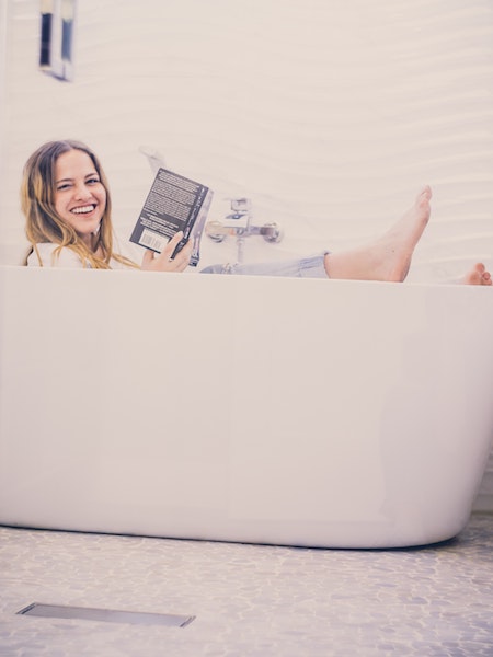 Smiling Woman Sitting in Bathtub Reading a Book