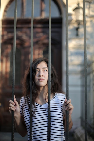 Woman Standing Behind Barred Gate