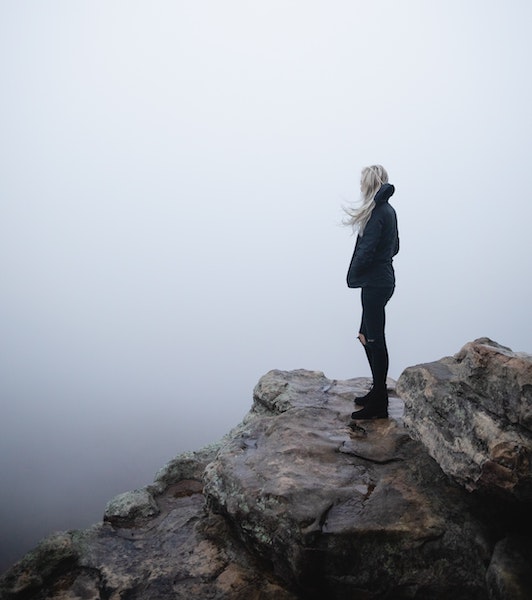 Woman Overlooking Fog While Standing on Rocky Cliff