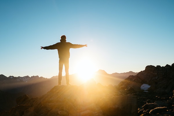 Person Standing on Mountain Top Overlooking Sunrise