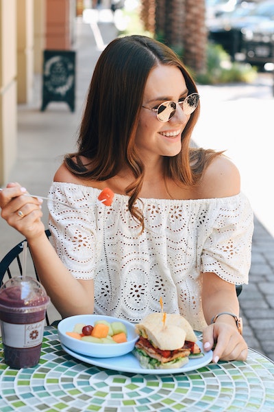 Smiling Woman Eating Fruit And Sandwich At Table