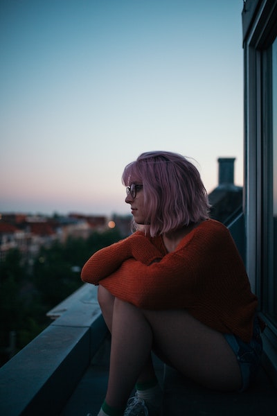 Pensive Woman Sitting On Balcony Overlooking Cityscape