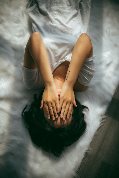 Person Laying on Bed with Hands Covering Face