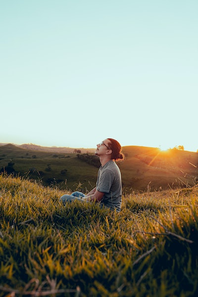 Man Sitting in Grassy Field With Eyes Closed