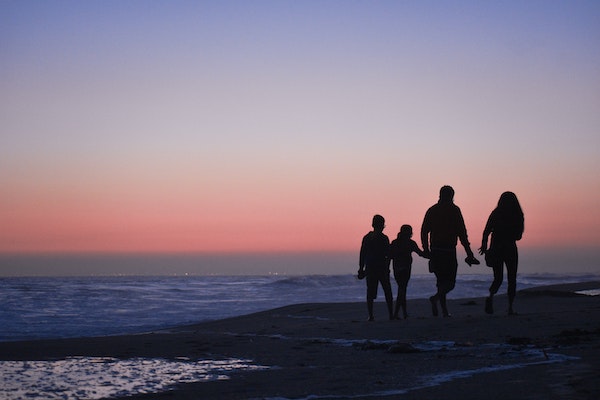 Family of Four Walking Together on the Beach at Sunset