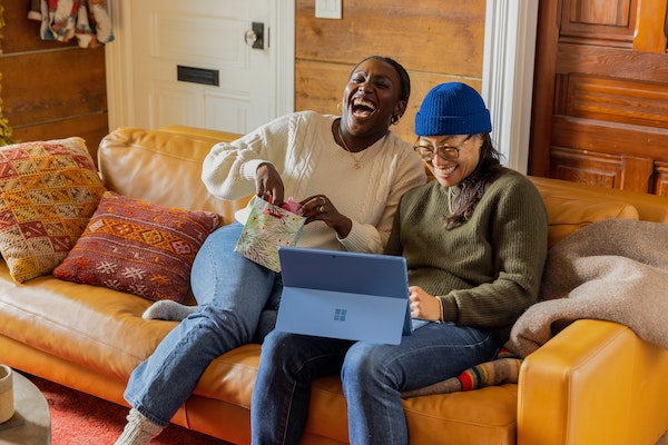 Two People Sitting on Couch Smiling, While Looking at Laptop